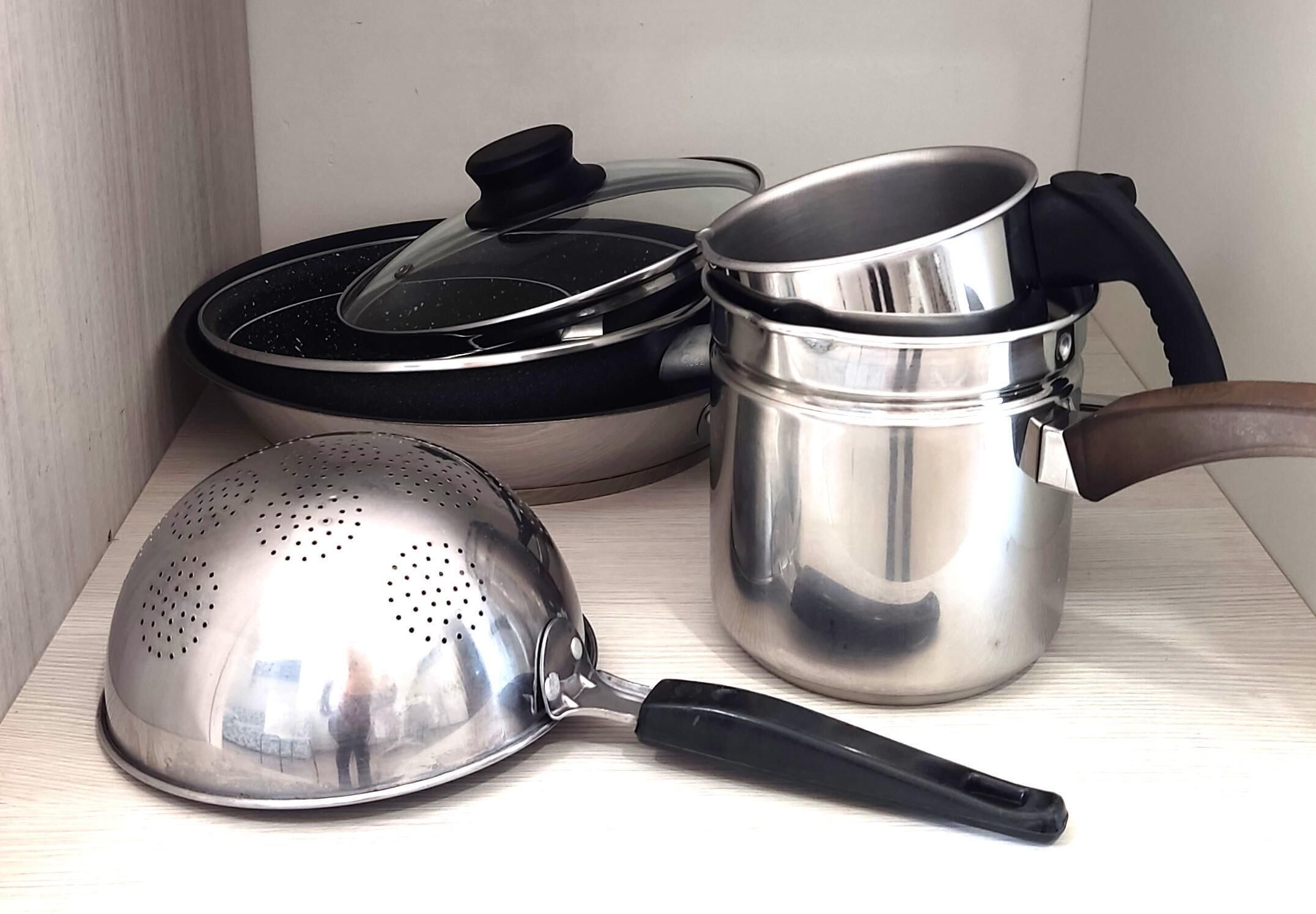 A kitchen shelf with a colander, a pot with a lid, and a pan.