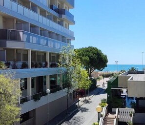 Un hotel de varios pisos con balcones, vista despejada al mar y un camino peatonal.