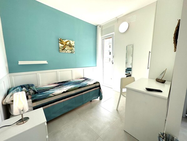 Un dormitorio con cama, una mesita de noche, una lámpara, un espejo y una obra de arte colgada en la pared.
