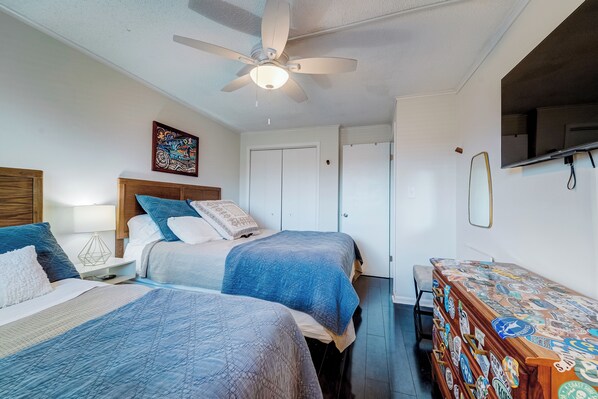 A bedroom with two beds, a ceiling fan, a TV, and a dresser with stickers.