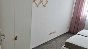 Une chambre avec une armoire, un lit, un luminaire fixé au mur et un rideau.