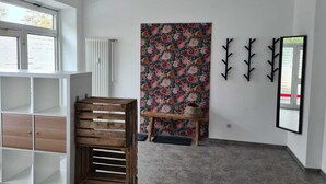 Une pièce avec un radiateur blanc, un banc en bois, un papier peint à motifs floraux et un porte-manteau noir.