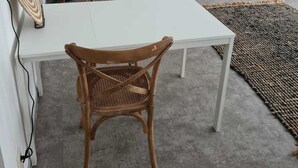 Un salon moderne avec une table blanche, deux fauteuils en osier, un téléviseur posé sur un meuble en bois et un élément décoratif rond fixé au mur.