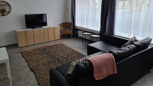 Un salon moderne avec un téléviseur posé sur un meuble en bois, un canapé noir, une petite table ronde et un fauteuil.