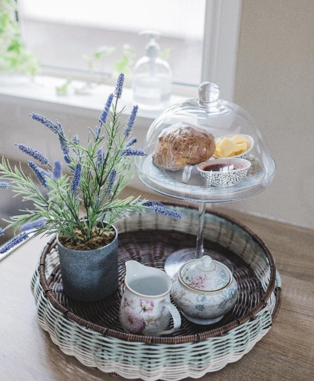 A tea set on a wicker tray with a potted lavender plant beside it.