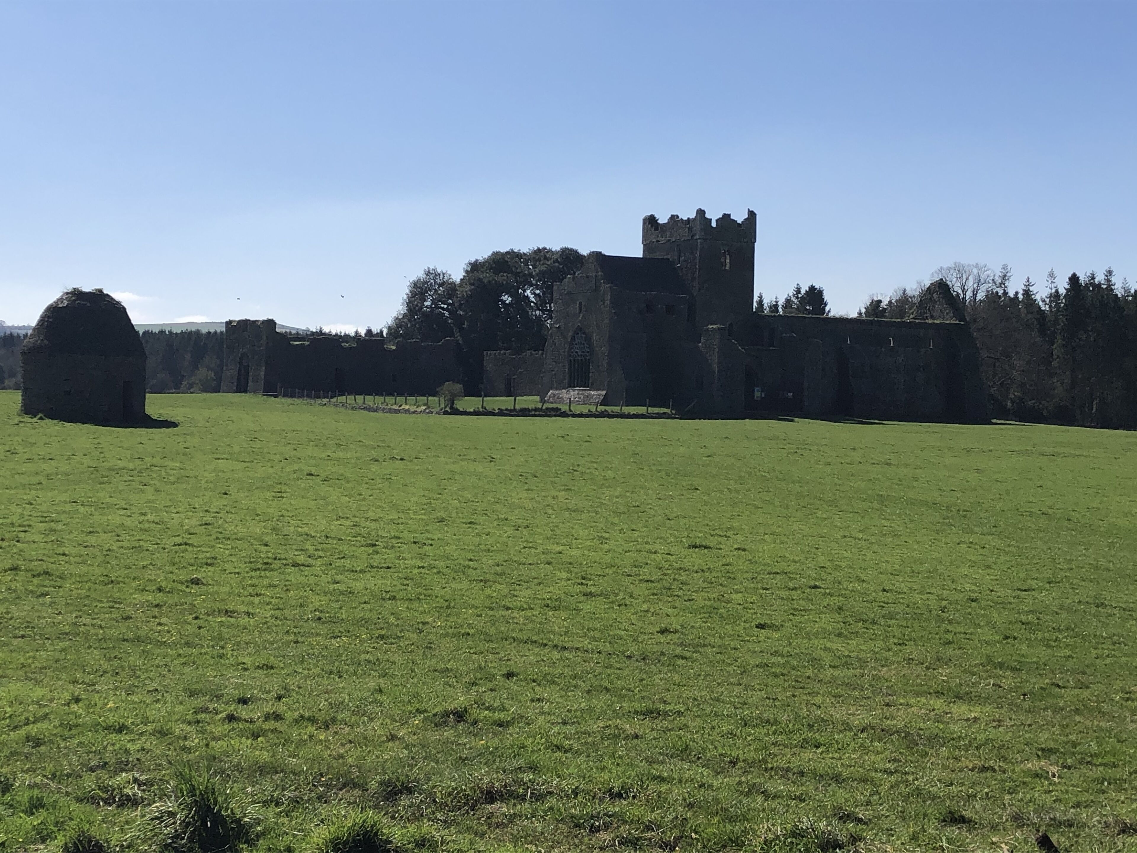 A large, open grassy field with a historic stone building featuring a prominent tower in the background.