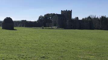 A large, open grassy field with a historic stone building featuring a prominent tower in the background.