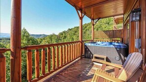 A wooden deck with a hot tub, wooden chairs, and a view of the mountains.