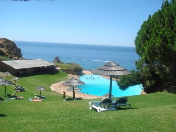 Un resort frente a la playa con piscina, sillas de descanso y sombrillas.