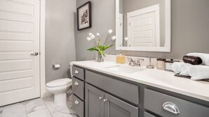 Et moderne badeværelse med toilet i hvid, grå kommode og et stort spejl.