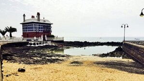 Un edificio costero con fachada de ladrillo rojo y ventanas amplias, ubicado cerca de una costa rocosa con un mar tranquilo al fondo.
