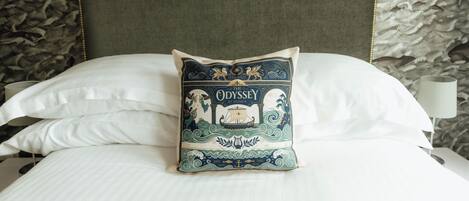 A bed with a decorative pillow featuring a nautical theme, a plain headboard, and a patterned wall behind.