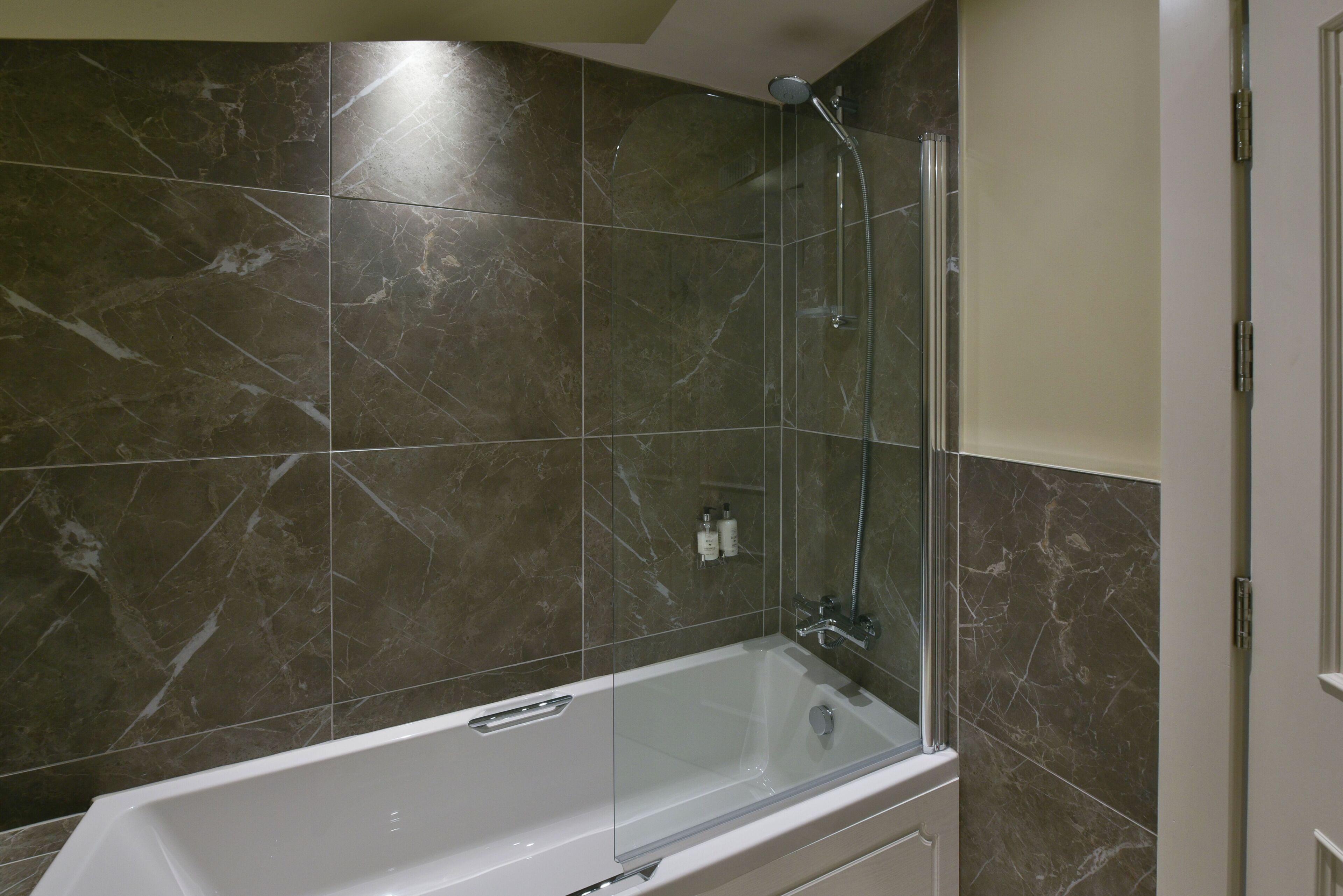A modern bathroom with a glass-enclosed shower, a white bathtub, and marble tiles.