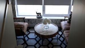 A room with a round wooden table, two leather sofas, a patterned rug, and a window with a decorative deer figurine. - The Seafield Arms Hotel Cullen – Self Catering (Buckie)