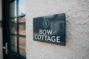A sign for "BOW COTTAGE" with a logo and text on a textured wall. - The Seafield Arms Hotel Cullen – Self Catering (Buckie)