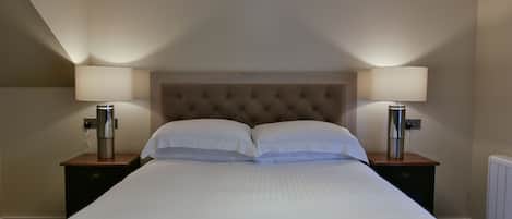 A neatly made bed with a tufted headboard, two bedside lamps, and a small wooden nightstand with a drawer.