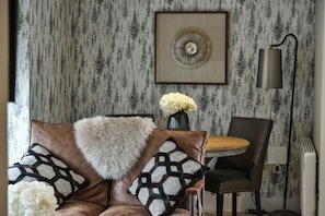 Una habitación con papel tapiz estampado, una mesa redonda con sillas, un sofá con cojines estampados y una lámpara fijada a la pared.