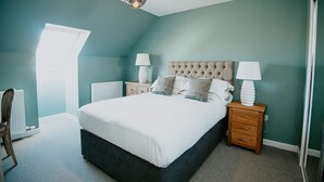 A bedroom with a large bed, two bedside tables with lamps, a radiator, and a window. - The Seafield Arms Hotel Cullen – Self Catering (Buckie)