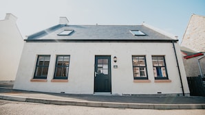 A two-story building with a white facade, a black door, and two windows on the upper floor. - The Seafield Arms Hotel Cullen – Self Catering (Buckie)