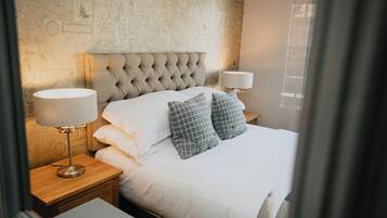 A neatly made bed with white linens and two checkered pillows, flanked by two bedside lamps on wooden nightstands.