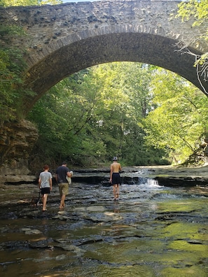 Eine Stebrücke über einem Bach, darunter gehen Menschen hindurch.