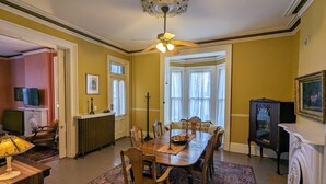 Ein Esszimmer mit Holztisch, Stühlen, einer Chandelierleuchtre und einem Erkerfenster mit Vorhängen.