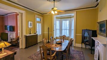 A dining room with a wooden table, chairs, a chandelier, and a bay window with curtains.