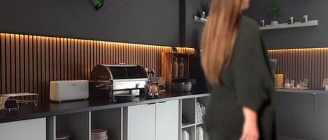 Une cuisine moderne dotée d’une machine à expresso intégrée, de meubles blancs et d’étagères où sont rangés les ustensiles de cuisine.