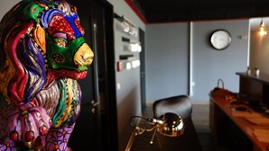 A colorful lion sculpture in a room with a desk, chair, and a clock on the wall.