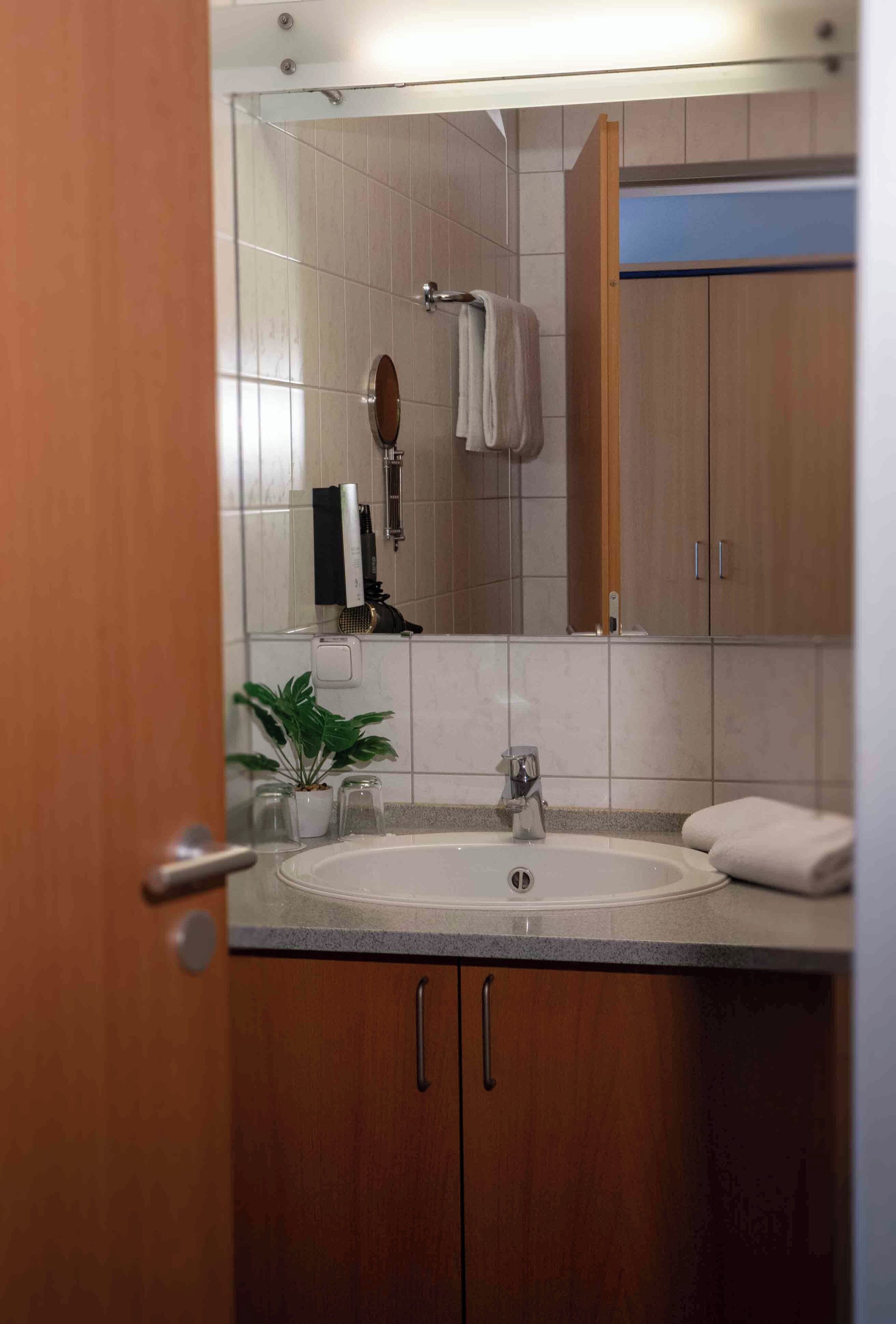 Een badkamer met een wastafel, spiegel, handdoekhouder en houten kasten.