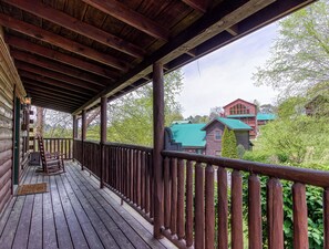 Une terrasse en bois avec une balustrade, un fauteuil à bascule et une vue sur un grand bâtiment doté d’un toit végétalisé.