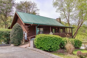 Une cabane rustique en rondins de bois, avec un toit en métal vert, une véranda et un jardin bien entretenu.