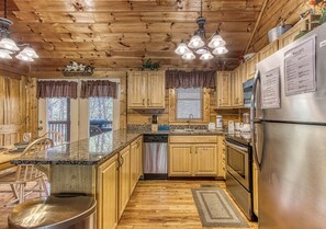 Une cuisine rustique, située dans une cabane en bois, avec des comptoirs en granit, des armoires en bois, un réfrigérateur en acier inoxydable et un four encastré.