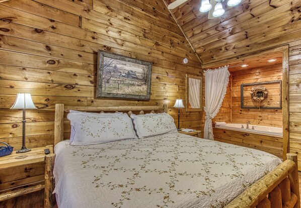 A wooden cabin-style bedroom with a large bed, two bedside lamps, a framed picture on the wall, and a welcome sign. - 2 King Bedroom Cabin with Private Hot Tub, Pool Table & Arcade (SEVIERVILLE)
