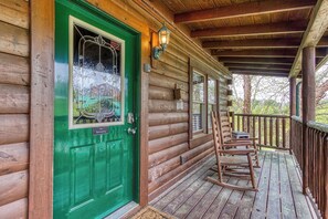 A wooden cabin with a green door, a porch with rocking chairs, and a wooden railing. - 2 King Bedroom Cabin with Private Hot Tub, Pool Table & Arcade (SEVIERVILLE)