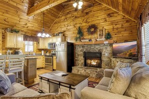 A cozy cabin interior with wooden walls, a stone fireplace, a kitchen with modern appliances, and a comfortable seating area. - 2 King Bedroom Cabin with Private Hot Tub, Pool Table & Arcade (SEVIERVILLE)