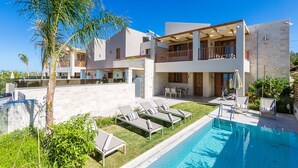 Ein modernes, zweistöckiges Haus mit Swimmingpool, Sitzgelegenheiten im Freien und einem Balkon.