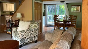 A cozy living room with a patterned sofa, a wooden coffee table, and a dining area with a table and chairs. A kitchen with cabinets and a toaster is visible in the background. - The Quiet Spot Cabin (Naples)