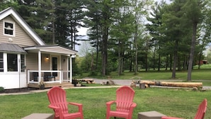 A cozy outdoor seating area with red Adirondack chairs and a fire pit, surrounded by a well-maintained lawn and a house with a porch. - The Quiet Spot Cabin (Naples)