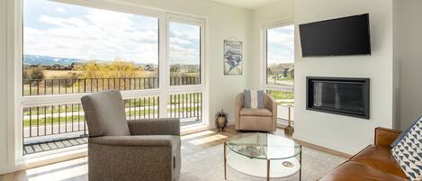 A spacious living room with large windows, a flat-screen TV, and a comfortable seating area.