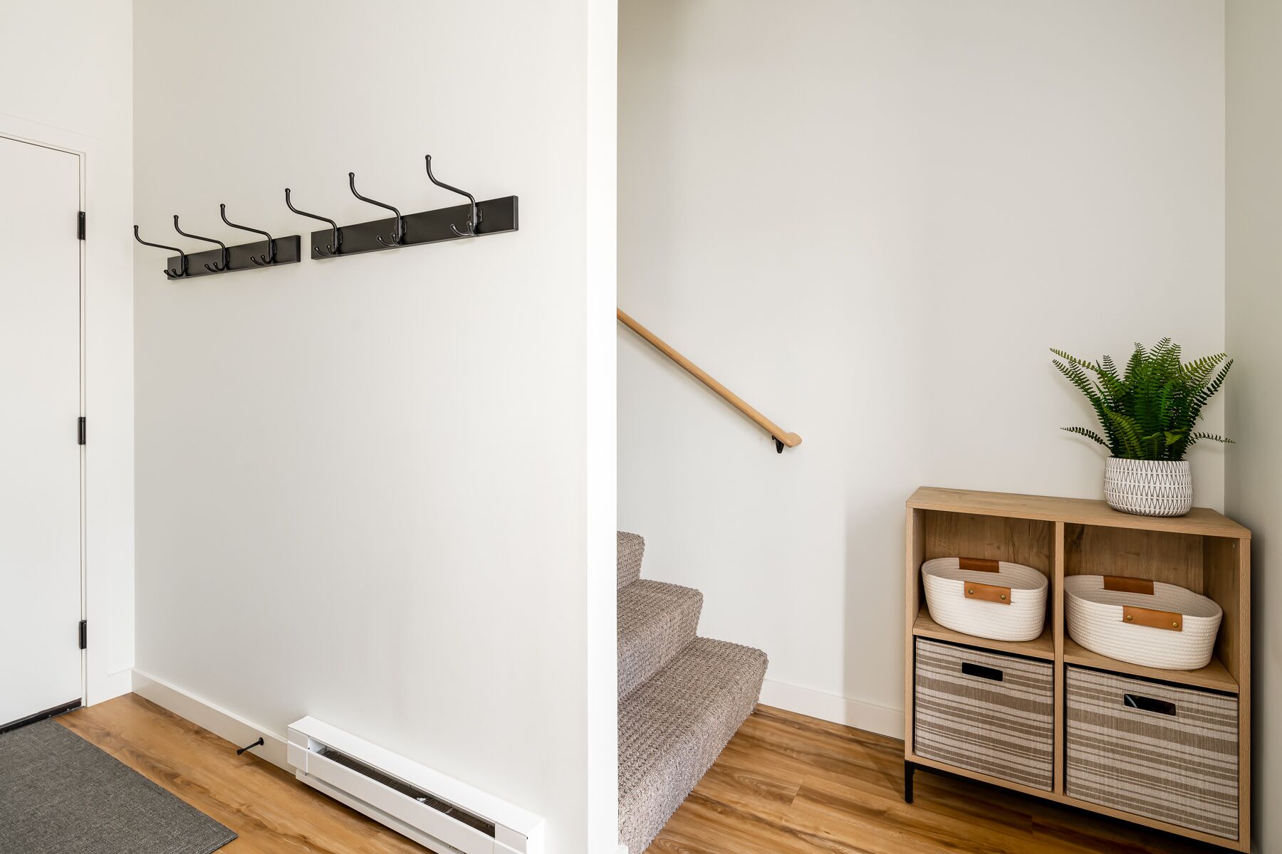 A hallway with a coat rack, a wooden bench with baskets, and a potted plant.