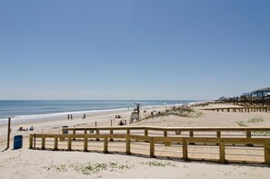 A beach with a wooden boardwalk, a lifeguard tower, and a clear blue sky. - 4 BR Townhouse with a Pool (Carolina Beach)