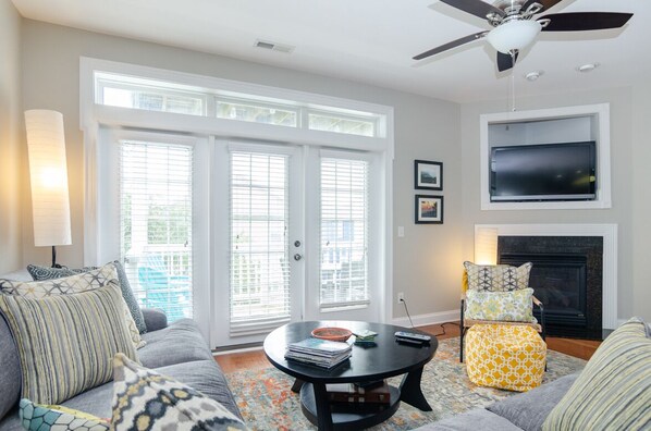 A living room with a sofa, coffee table, and ottoman, a fireplace, and a TV mounted on the wall. - 4 BR Townhouse with a Pool (Carolina Beach)