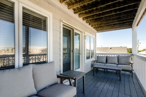 Una terraza techada al aire libre con un sofá y una mesa, ventanas amplias con persianas y vista a la ciudad.