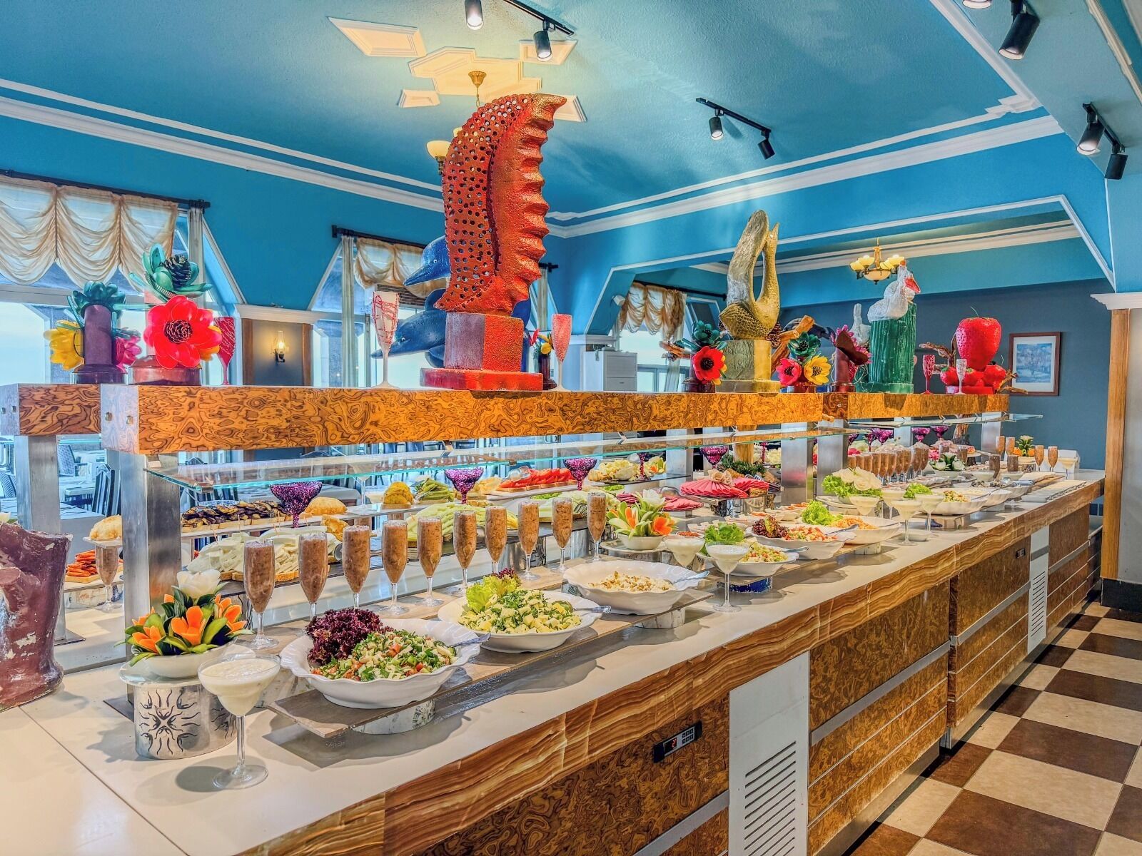 Een buffet met diverse gerechten en drankjes, een decoratief plafond en een geruit vloertje.