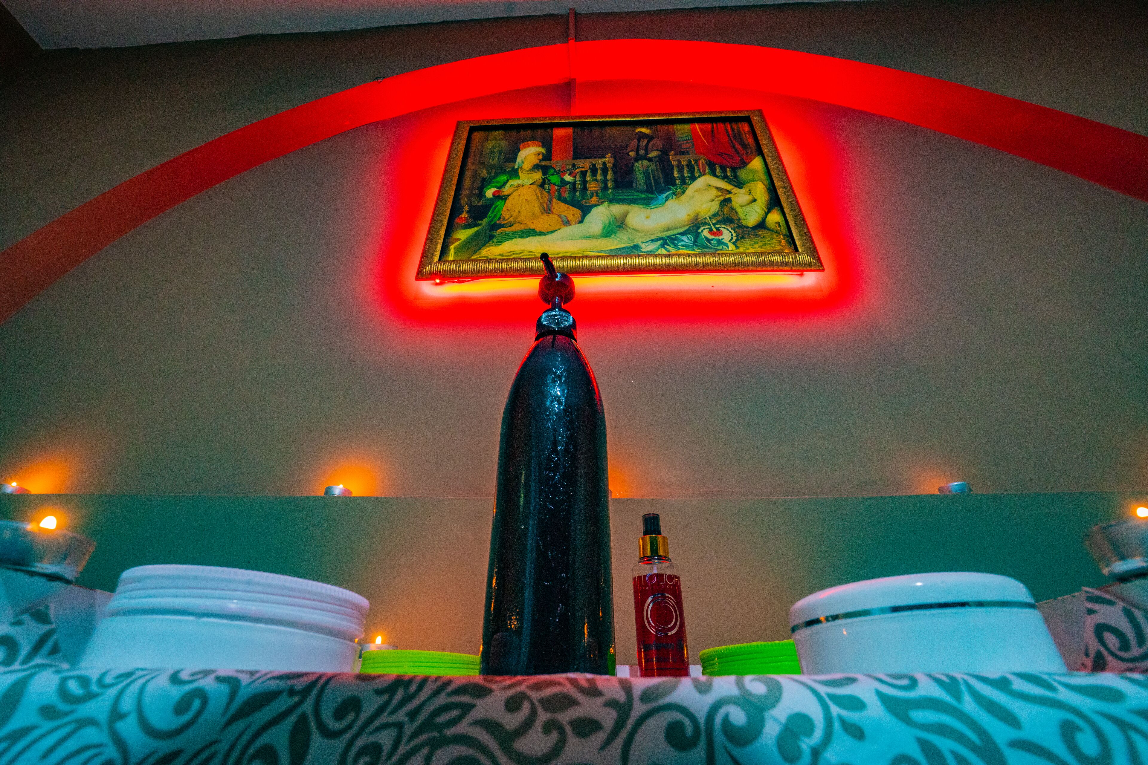 A room with a painting on the wall, a bottle, and a vase on the table.
