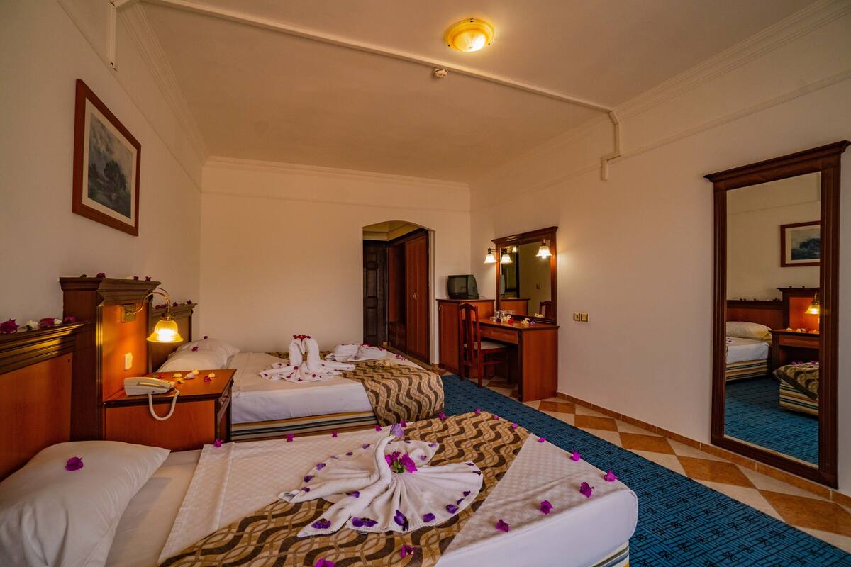 A hotel room with two beds, a desk, a chair, a mirror, and a telephone.