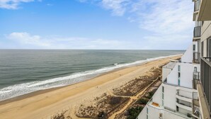 Vista costera con playa y océano, un edificio con balcones y cielo despejado.