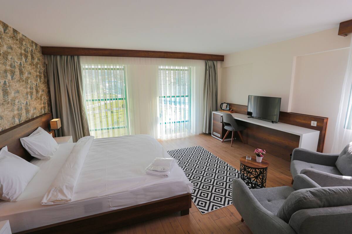 A hotel room with a large bed, a desk, a television, and a seating area.