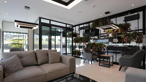 A modern living room with a sofa, armchairs, and a coffee table. There are large windows, indoor plants, and a staircase. - Avwan Hotel Cigli (Izmir)